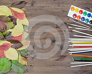 Autumn leaves paints pencils and brushes on wooden background