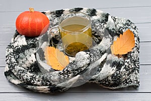 Autumn leaves, pumpkin, a cup of green tea in a variegated black and white scarf on a gray wooden background. A woolen