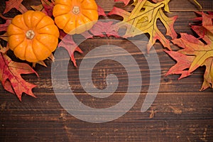 Autumn leaves and pumpkins on a wooden background forming a bor