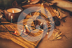 Autumn leaves, spices and candle on cozy knitted sweater in warm yellow lights. Happy Thanksgiving and Halloween, celebrating