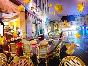Autumn leaves street cafe tables in Old Town Of Tallinn town square ,evening city lights red tables and chair windows reflection