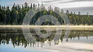 Autumn with mirrored pine forest and misty lake. Fog rises above the water at dawn. Finland