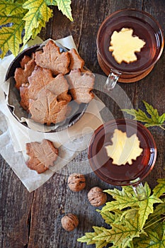 Autumn mood: cinnamon cookies in form of maple leaves, two cups of tea and yellow leaves