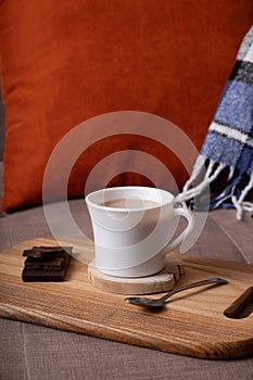 Autumn mood composition with cup of cocoa and chocolate, plaid and books on sofa background. Hot drink in autumn concept