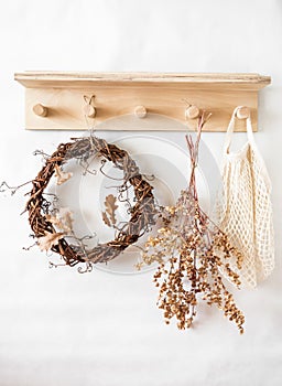 Autumn mood still life - wooden shelf with a vine wreath, dried flowers, fabric bag in a bright room. Cozy eco home style