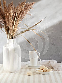 Autumn morning table with coffee cups, macarons and dried reeds in vase.