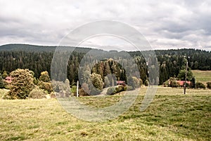 Autumn mountain countryside with meadow, few houses, trees and hills covered by forest