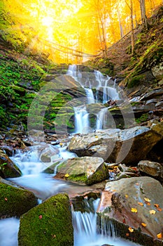 Autumn mountain waterfall stream in the rocks with colorful fallen dry leaves, landscape
