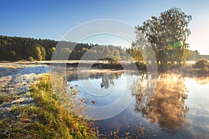 Autumn nature. Fall landscape. Calm scene on river side in misty morning at sunrise. Beautiful october foggy morning. Trees on