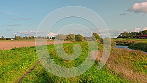 Autumn nature landscape view. Small river along agriculture field merging with blue sky.