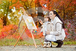 Autumn nature, mom and daughter paint a picture in a park of autumn leaves, painting a Little Child, Child Creativity