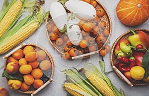 Autumn orange, yellow, red vegetables and fruits set, apricots, cherry tomatoes, corn, etc. in wicker trays on gray linen