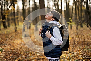 Autumn outdoor portrait of teenager boy with backpack in forest look up