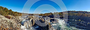 Autumn panoramic view of the mountain river. Stormy water flows among high stones and rocks under a blue sky