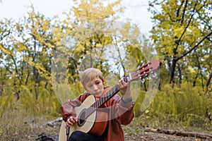 in autumn in the park a boy plays the guitar looks at the strings and tunes the guitar