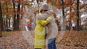 Autumn park with happy senior man and woman entering walking to each other hugging kissing. Side view portrait of loving