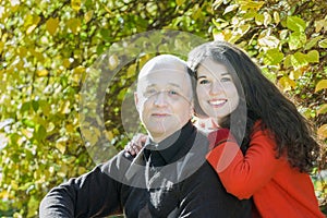 Autumn park outdoor family portrait of smiling adult daughter hugging her senior father