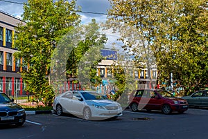 An autumn picture of a falling asleep city, yellowing trees against a cloudy sky. Car near the new school.