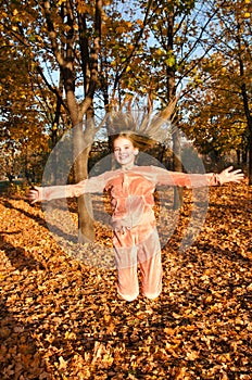 Autumn portrait of adorable smiling little girl child preteen having fun and jumping in leaves in the park