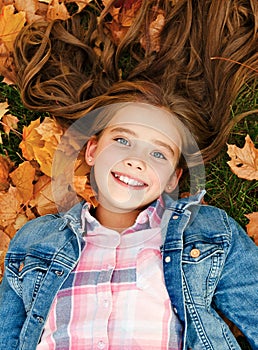 Autumn portrait of adorable smiling little girl child preteen lying in leaves in the park