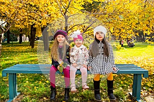 Autumn portrait of beautiful children on the bench. Happy little girls with leaves in the park in fall.