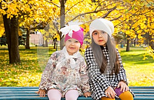 Autumn portrait of beautiful children on the bench. Happy little girls with leaves in the park in fall.