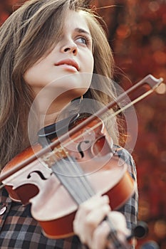 Autumn portrait beautiful woman enjoying playing violin on a background of red leaves, romantic girl engaged in art on nature,