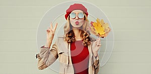 Autumn portrait of beautiful woman with yellow maple leaves, female model blowing red lips sending sweet air kiss