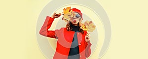 Autumn portrait of beautiful young woman model with yellow maple leaves blowing her lips with lipstick wearing red french beret on