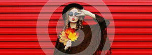 Autumn portrait of beautiful young woman with yellow maple leaves blowing her lips with lipstick wearing brown knitted poncho,