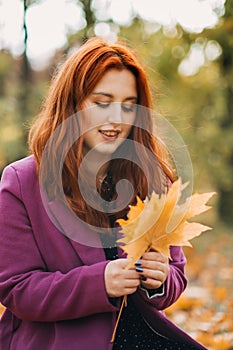 Autumn portrait of candid beautiful red-haired girl with fall leaves in hair.