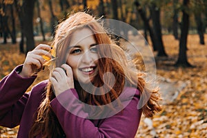 Autumn portrait of candid beautiful red-haired girl with fall leaves in hair.