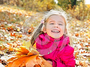 Autumn portrait of cute laughing little girl with maple leaves