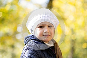 Autumn portrait of cute little blond girl in white hat. Beautiful smiling child having fun outdoors on a warm fall day