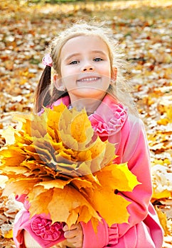 Autumn portrait of cute smiling little girl with maple leaves