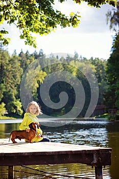 Autumn portrait of a girl child with a dog red Dachshund on the bridge in Sunny Park. Friends sit on the bridge by the water