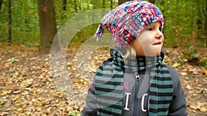 Autumn portrait of a girl in a hat and scarf. The child walks in the forest.