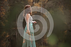 Autumn portrait of a girl standing in a forest lake.