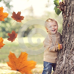 Autumn portrait of happy child playing having fun with flying yellow maple leaves