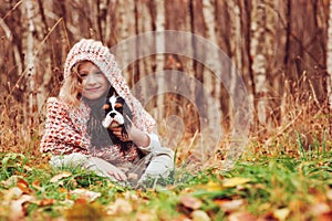 Autumn portrait of happy kid girl playing with her spaniel dog in the garden