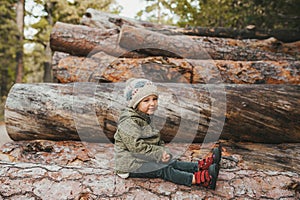 Autumn portrait of little girl in the autumn park on stack of logs. Side view