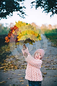 Autumn portrait of little girl holding beautiful umbrella covered with yellow maple leaves