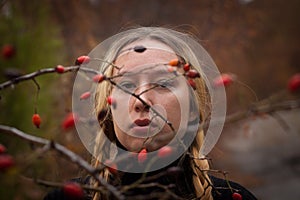 Autumn portrait of pensive young woman behind the branches of a rosehip bush