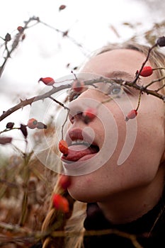 Autumn portrait of pensive young woman behind the branches of a rosehip bush