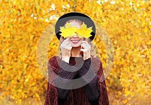 Autumn portrait smiling woman wearing a black hat and knitted poncho over sunny yellow leaves