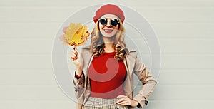 Autumn portrait of smiling young woman with yellow maple leaves wearing red french beret over gray