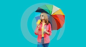Autumn portrait of stylish young woman holding colorful umbrella and drinks fresh juice wearing pink jacket on blue background