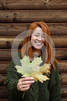 Autumn portrait young adult woman in sweater with maple leaf