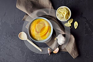 Autumn pumpkin soup in a bowl with spoon with fresh garlic and wheat croutons on dark grunge background.