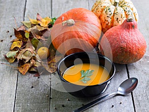 Autumn pumpkin soup in black bowl on natural wooden table.